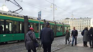 Spårvagnarna i Helsingfors väntas stå stilla ända till åtminstone klockan 18 på fredag. Människor vid Domkyrkan