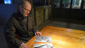 Börje Wikner tittar på gamla bilder från hemstället. På bilden nedan syns den gamla träbyggnaden som senare har ersatts av ridskolans manege. Börje Wikner kom till Porkala som 6-åring år 1957.