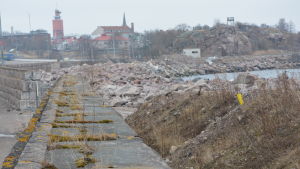 Sprängsten lagras på land mellan stenmuren och havet. Sprängstenen ska bli en vågbrytare i Hangö hamn. Stenbumlingar väntar på stranden för att bli vågbrytare i Västra hamnen i Hangö.