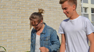 Lina Trygg och Jonatan Wikström. Ung flicka och pojke utomhus framför skolbyggnad.