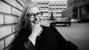 Anita Kurvinen istuu penkillä ja hymyilee suoraan kohti kameraa.