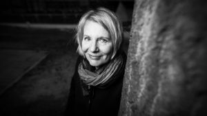 Nainen, Heidi Köngäs hymyilee kameralle puunrungon takaa.