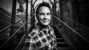 Mies, Matti Kajander poseeraa ja hymyilee kameralle rappukäytävässä.