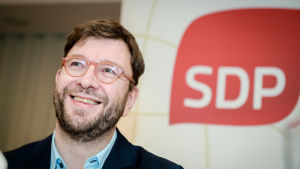 Timo Harakka var först med att utmana Antti Rinne. Timo Harakka med SDP:s logo i bakgrunden.