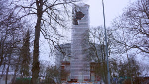 Presenningarna runt kyrkan har flera gånger flugit bort på grund av stormvindar. Kristinestads kyrka intäckt i presenningar.