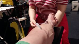 Blodgivningstillfälle, där en person från Blodtjänst övervakar processen då blod doneras från en arm.