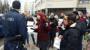 Prästen Marjaana Toiviainen försöker övertyga polisen om att hon måste få kontakt med asylsökandena inne i polishuset. Demonstranter utanför polishuset i Böle, som protesterar mot att asylsökande utvisas från Finland.