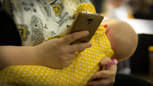 Amning på offentliga platser ifrågasätts i sociala medier. Äiti selaile kännykkänsä ja samalla rintaruokii vauvaa helsingin lapsimessuilla