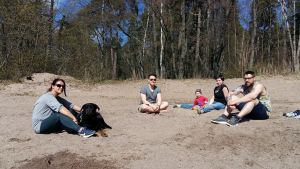 De unga tyskarna tyckte det var ett jättefint initiativ att städa stränder. Fyra unga personer med ett litet barn och en hund sitter på sandstranden och njuter av vårsolen.