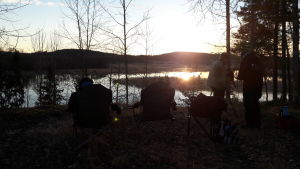 Luontotoimittajat ovat asetelleen retkituoleja järven rannalle. Aurinko nousee.