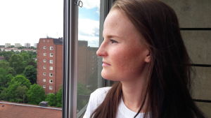 Madelene Orre har en lägenhet till låns för tillfället. Hon är bostadssökande och har under flera år haft många olika boenden. - Man hittar till slut om man orkar leta, säger hon. Madelene på balkong i högt hus, andra höghus i förort i bakgrunden.