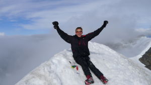 Aron Anderson på toppen av Kebnekaise, år 2013. Aron Anderson sitter på toppen av Kebnekaise. Bergskammar syns i bakgrunden.