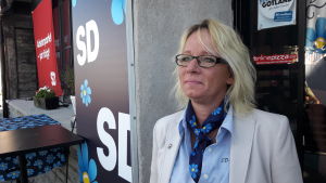 Carina Herrstedt tror att det finns en stor krompomissvilja inom SD, men hon vågar inte lova att det gäller migrationspolitiken. Carina Herrstedt i profil framför SD-logga på husfasad.