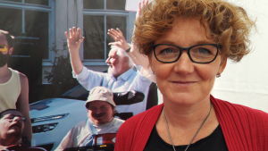 JAG:s medlemmar beslutar att lämna Almedalen, på grund av nazisternas närvaro. Cecilia Blanck framför affisch med medlemmar inom JAG, som skrattar och sträcker händerna glatt upp i luften.