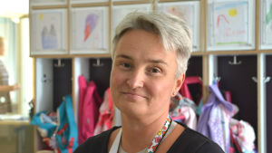 Maria Johansson. Närbild på Maria Johansson. I bakgrunden teckningar och barns utekläder