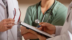 Läkare som tittar på en patientjournal. Inga ansikten syns, bara händer och läkarrockar.