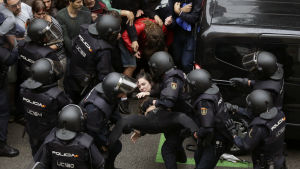 Oroligheter utanför en vallokal i Barcelona under folkomröstningen den 1 oktober. Spansk kravallpolis bär bort en ung kvinna.
