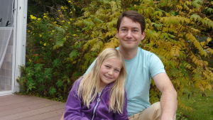 Ulf och Felicia Tigerstedt. En pappa sitter med sitt barn framför en buske vars löv börjat gulna.