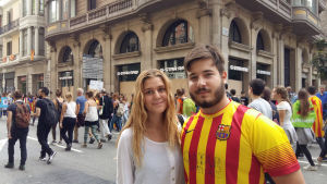 Ariadna Basso och David Hill. Två personer tittar in i kameran, i bakgrunden folkvimmel och demonstrationer