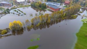 Vattnet från Esbo å har stigit och nästan nått två skolbyggnader: uppe i vänstra hörnet på bilden syns Kirkkojärven koulu, den röda byggnaden till höger är gymnasiet Kuninkaantien lukio. Stora delar av Kyrkträsk i Esbo ser ut som en sjö.