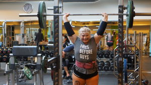 Sara Dahlström. Sara Dahlström står i ett gym och lyfter en stång med vikter ovanför sitt huvud. På hennes tröja står det "Fries before guys".