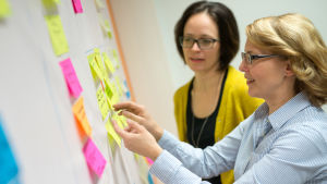 Yleisötutkija Anne Hyvärilä ja Älykäs data ja asiakkuus -tiimin päällikkö Eija Moisala seisovat kanban-taulun ääressä.