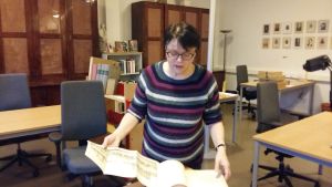 Eva Costiander-Huldén bläddrar i Johan Gadolins bok kvinna med kort mörkt hår och glasögon bläddrar i gammal bok