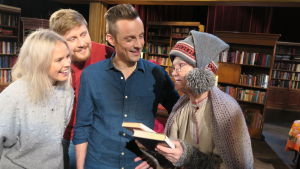 BUU-ledarna åker till Korvatunturis bibliotek i årets julkalender. Där träffar de bibliotekstomten (Sue Lemström). Tre personer ser leende mot en tomte