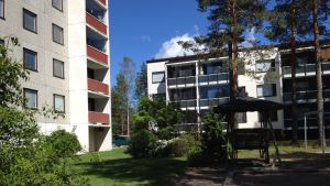 Eldsvådan bröt ut i en lägenhet på översta våningen i huset till vänster. Ett höghus på fem våningar och ett bostadshus på tre våningar vid gräsplan. På bilden syns även en trädgårdsgunga.