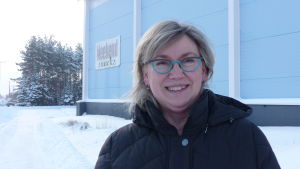 Ebba Dåhli. En kvinna med blont hår och glasögon står framför en produktionshall i Kaskö.