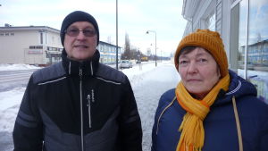 Yngve och Margareta Karlå. En man klädd i en svart mössa och svart jacka. Bredvid honom en kvinna med orange mössa och halsduk i samma färg.