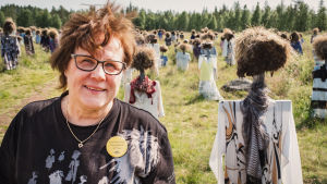 Om somrarna är det här ett fönster ut mot världen, säger Ritva Huttunen. Hit kommer människor från många olika länder, så jag får öva mig på mina språkkunskaper, och jag lär mig alltid något nytt. Hiljainen kansa -teoksen yhteydessä toimivan Niittykahvilan pitäjä Ritva Huttunen heinäseiväshahmojen keskellä.