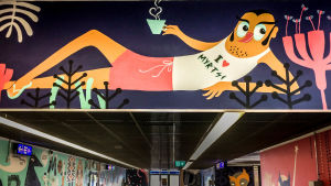 Myyrmäen juna-asemalla seinämaalaus, jossa loikoilee mieshahmo, jolla paita jossa teksti I love Myrtsi.