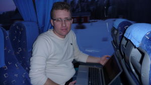 Andreas Forsbäck En man med glasögon sitter i en buss med en dator i famnen.