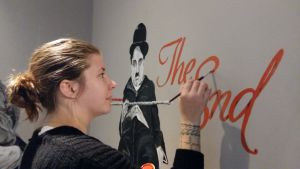 Johanna Karvonen. Johanna Karvonen målar Charlie Chaplin och The End på väggen i foajén på en biograf.