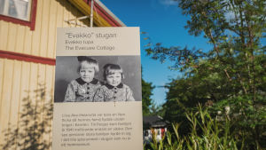 I Gamla Malmen finns det också ett litet museum tillägnat dem som evakuerades från Karelen. Kyltti, jossa vanha mustavalkoinen valokuva, jossa kaksi pikkutyttöä ja teksti Evakko-stugan, Evakko tupa, taustalla keltainen puutalo.