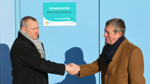 Vesa Heikkonen och Patrick Wackström skruvar upp skylten på det nya biogasverket och skakar sedan hand. Biogasanläggning invigs