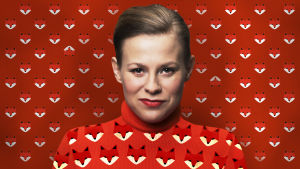 Kuvassa näyttelijä Emmi Parviainen punaisessa kettukuvioisessa paidassa, taustalla sama punainen kettukuviollinen tapetti.