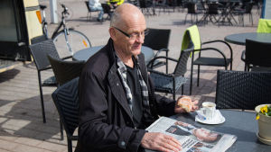 Stadsplaneringschef Eero Löytönen tar en kaffe på torget. bild på en man som sitter och läser en tidning