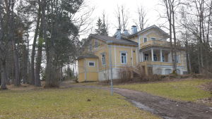 Grantorp sett från stranden. Ett gult hus med vita knutar på en kulle. Det heter Villa Grantorp.