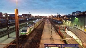 Åbo centraljärnvägsstation. Ett grönvitt tåg är klart att starta från Åbo järnvägsstation. I bakgrunden finns Logomo och gångbron som byggs över järnvägen.