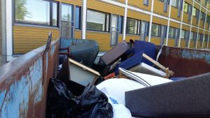 En fåtölj, säng och bokhylla är slängda på ett flak ned annat skräp utanför en studentbostad.
