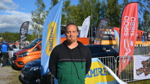 Oskar Kurri vid tävlingsområdet. Oscar står vid evenemangstält i solens sken.