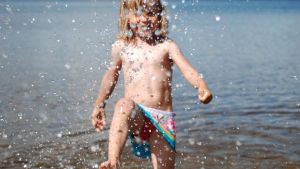 Det är viktigt att ge barn möjligheten att vara i vattnet och öva simning. En flicka som plaskar i vattnet på en strand.