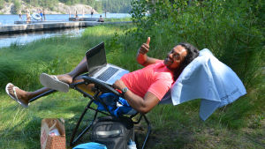 Ragha skriver på sin pro gradu i skuggan. Man sitter i solstol med bärbar dator i famnen.