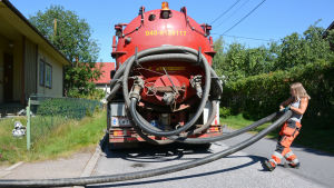 Ibland är det tungt att handskas med slangarna, men Isabelle Rio har utvecklat egna strategier för att få det att fungera. Kvinna drar sugslang till slambilen.