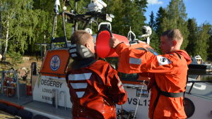 Till sist ska våtdräkten sköljas av med sötvatten. En man i röd overall häller vatten ur en hink på en annan man i röd overall.
