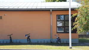 Sjundeå svenska skola. En bild på ett hus. Framför huset står tre cyklar i en cykelställning och brevid huset växer rönnbär.