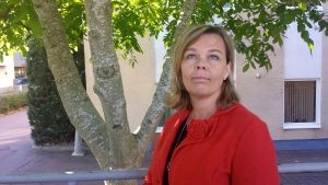 Viking Lines informationsdirektör Johanna Boijer-Svahnström säger att det är tryggt att åka båt. Rederiet har uppmärksammats för deras smittskyddsarbete mot coronaviruset. En blond kvinna i röd kavaj står på gatan under ett träd med tre stammar och blickar uppåt.