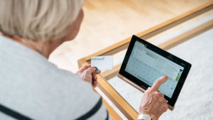 En äldre dam som loggar in på sin nätbank. Nainen kirjautuu tabletilla verkkopankkiin